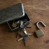 Ключі, що висипаються з металевої скриньки, і відкритий навісний замок на столі