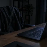 Нічний робочий стіл: відкритий ноутбук, холодна кава й худі на порожньому стільці