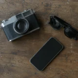 Вінтажний фотоапарат, смартфон і чорно-сонцезахисні окуляри на дерев’яній поверхні