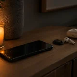 Світла свічка, смартфон і бездротові навушники на деревʼяній тумбі