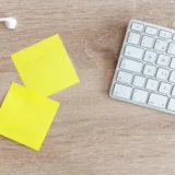 Верхній план робочого столу з клавіатурою, навушниками і жовтими нотатками