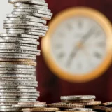 Стовпчик зі стосом срібних та золотих монет на тлі розмитого годинника