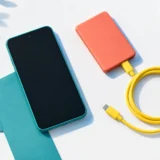 Туркуазовий смартфон з чохлом поруч із помаранчевим павербанком і жовтим кабелем